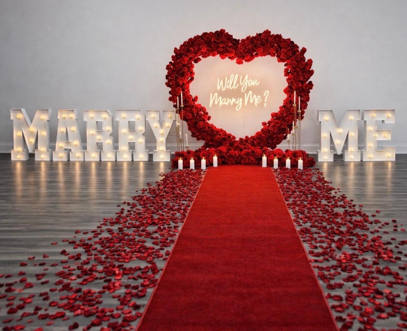 Indoor proposal package setup with red heart arch, Marry Me marquee letters, candles and rose petals in Chicago