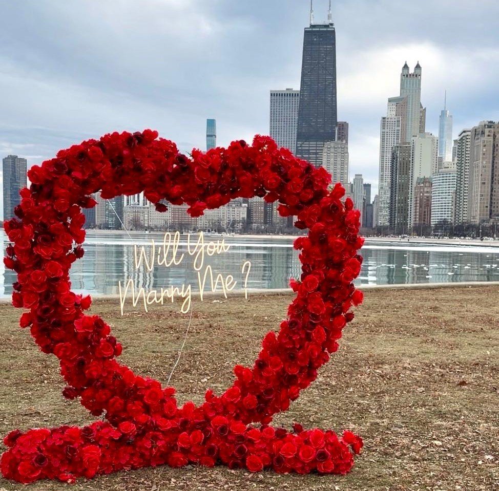 Heart-shaped floral arch proposal setup with Marry Me sign